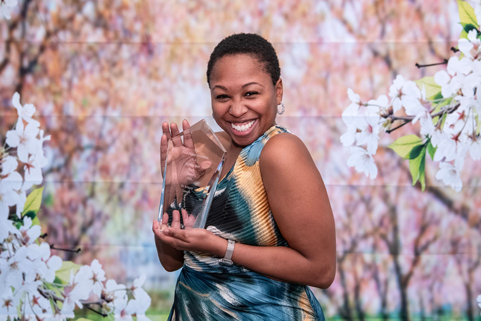 Brittany Conors holds an award and smiles for a photo in front of a floral background..