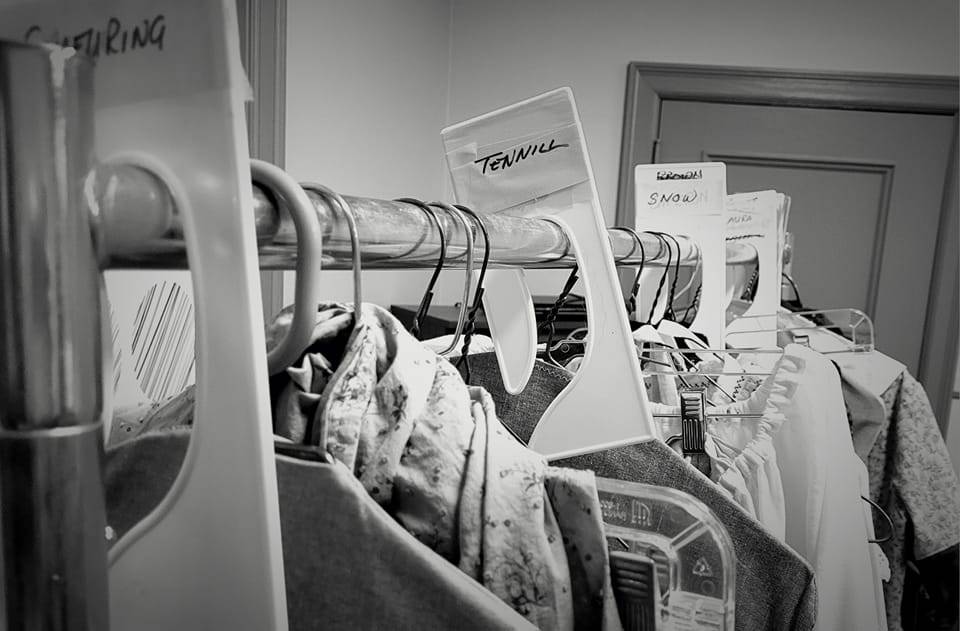 Costumes for "Into the Woods" A black and white photo of a rack of costumes with a divider labeled "Tennill"