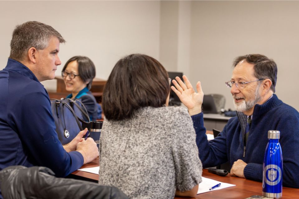 a man crouched talking to two participants sitting at a desk
