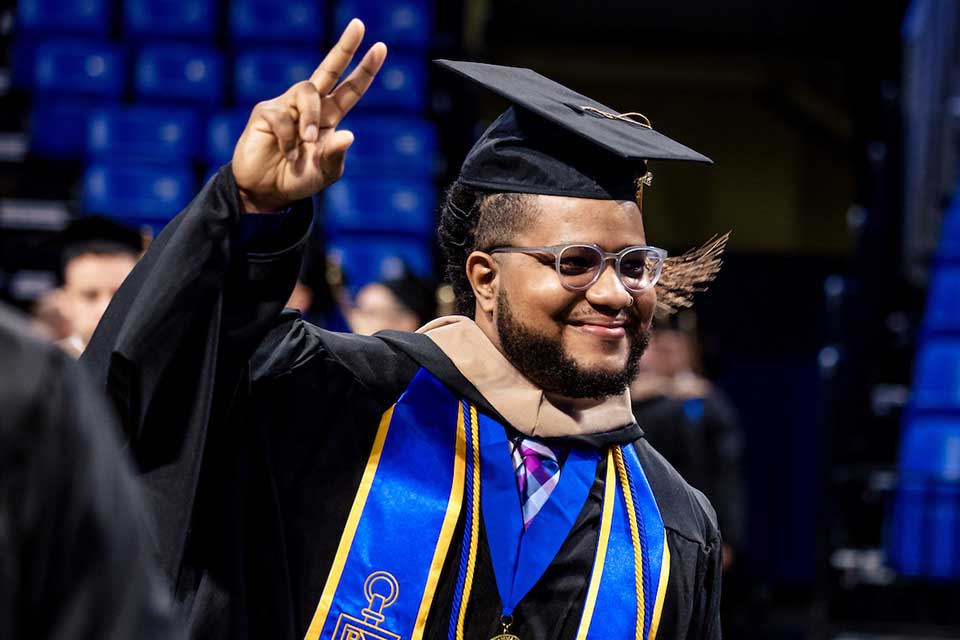 Midyear commencement graduate A graduate in a cap, gown and stole waves to a crowd at SLU midyear 22 commencement