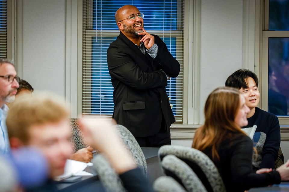 A seminar leader stands in a classroom and smiles.