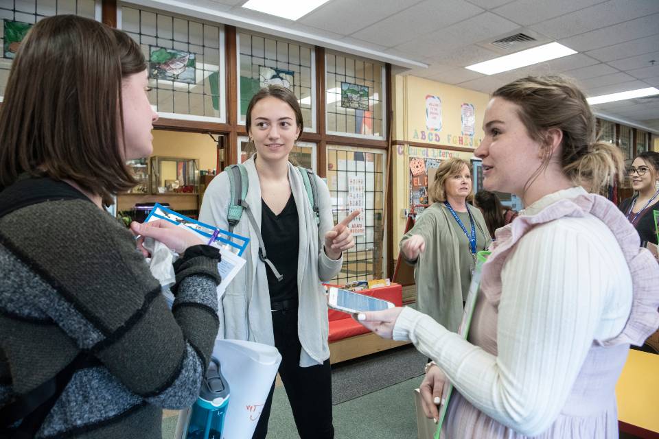 Three student teachers stand in a school classroom and talk.