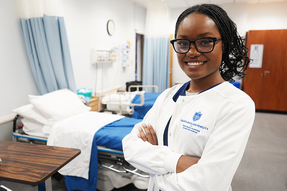Prosperity Meade poses for a photo wearing a white lab coat in a nursing classroom.
