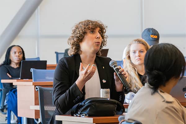 A woman sits at a table in the courtroom at Scott Hall, asking a question with a wireless microphone in her hand.