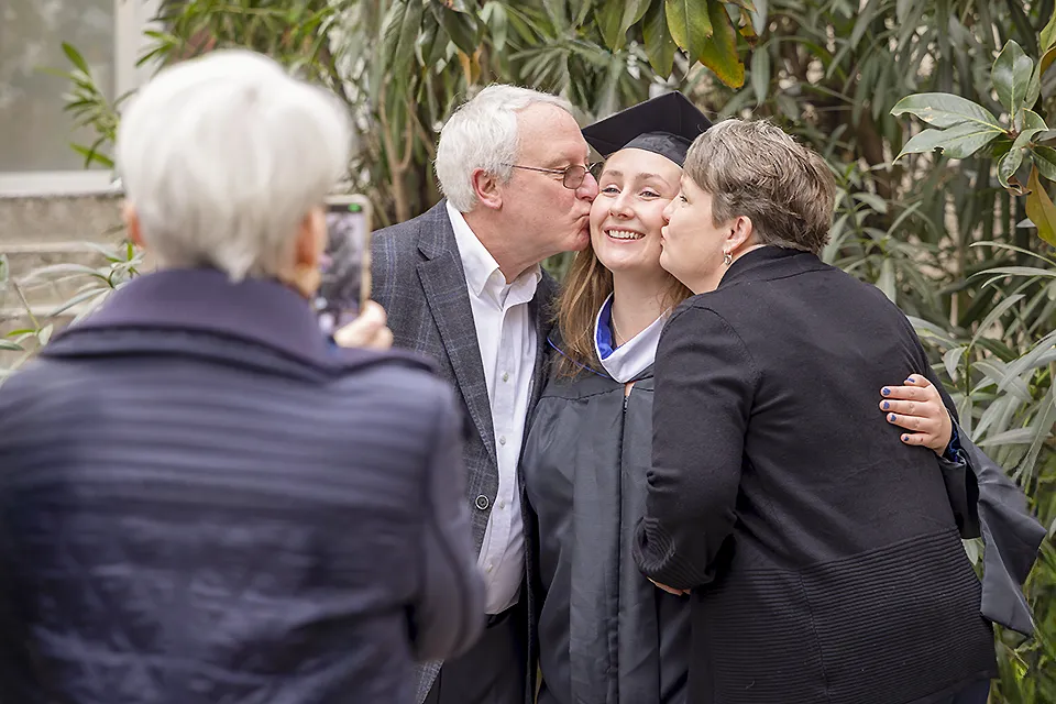 A woman hugs a participant in a graduation ceremony and looks up at the sky, while others mill around the area.