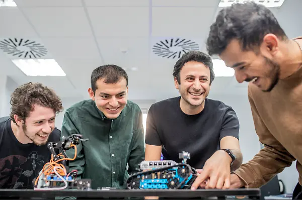 A student, dressed in a graduation gown, shakes hands with a SLU faculty members on stage during commencement. American and Spanish flags are in the background.