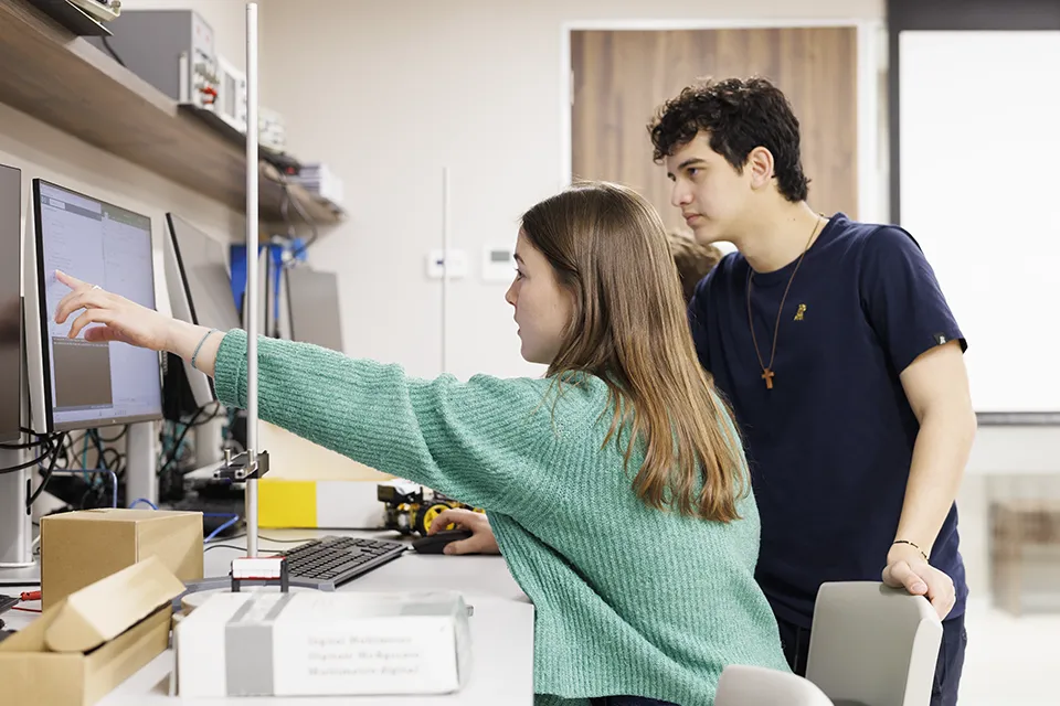 Two students talk to a professor while looking at a laptop.
