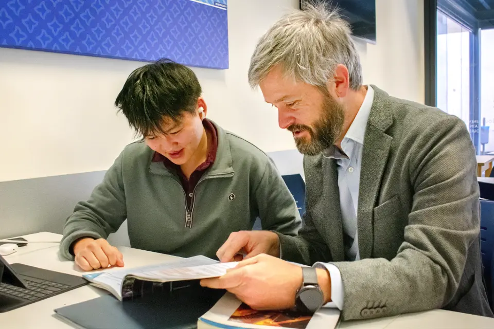 A teacher and a student look with interest at a book on the table.