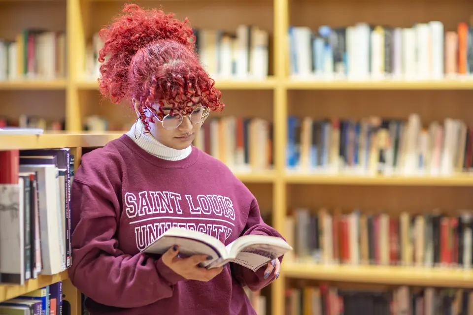Academic Minors Student stands in front of book shelves, holding a textbook.