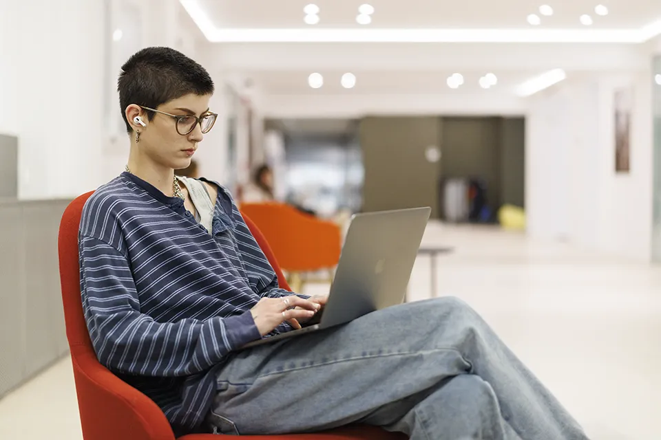 A student sitting on a chair using a laptop.