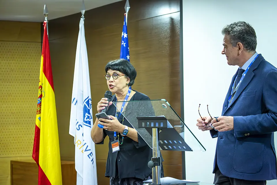 SLU-Madrid and Chaifetz School of Business Reflect on SLU’s Mission in Madrid Woman with microphone reading script off her phone introduces keynote speaker on stage in auditorium.