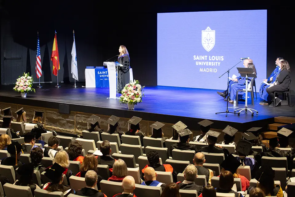 Commencement speaker Christine Amour-Levar addresses graduates and attendees on Friday, May 10. Woman talks at podium on stage in front of crowd in auditorium.