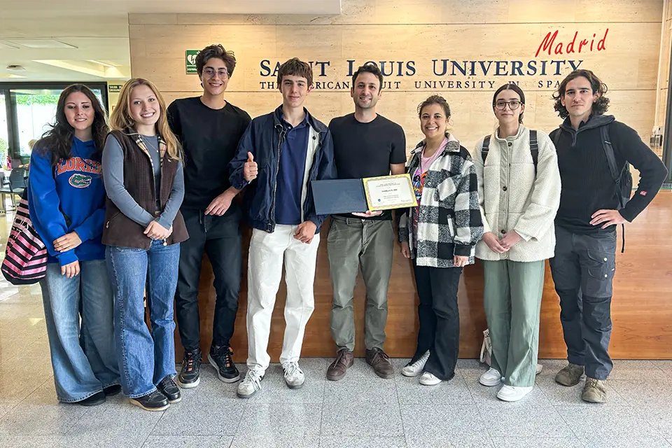 El Mir (center) poses with his students in front of the San Ignacio Hall reception desk. Photo by Isaiah Voss. A group of people posing for a photo while the man in the middle holds a certificate.