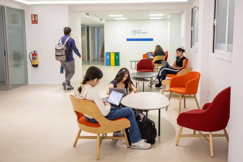 Students in lounge area in Manresa Hall. Students sitting in chairs studying on laptops in a lobby area of the building.