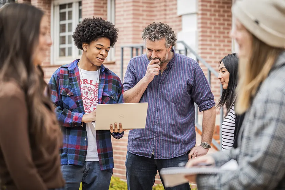 Program director Hamish Binns with students outside Padre Arrupe Hall. Professor with students looking at a laptop while standing outside.