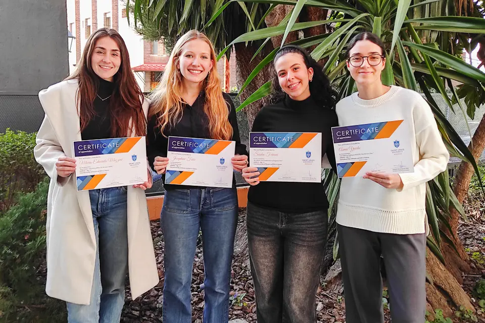 Four women hold certificates and smile for photo with plants in the background.
