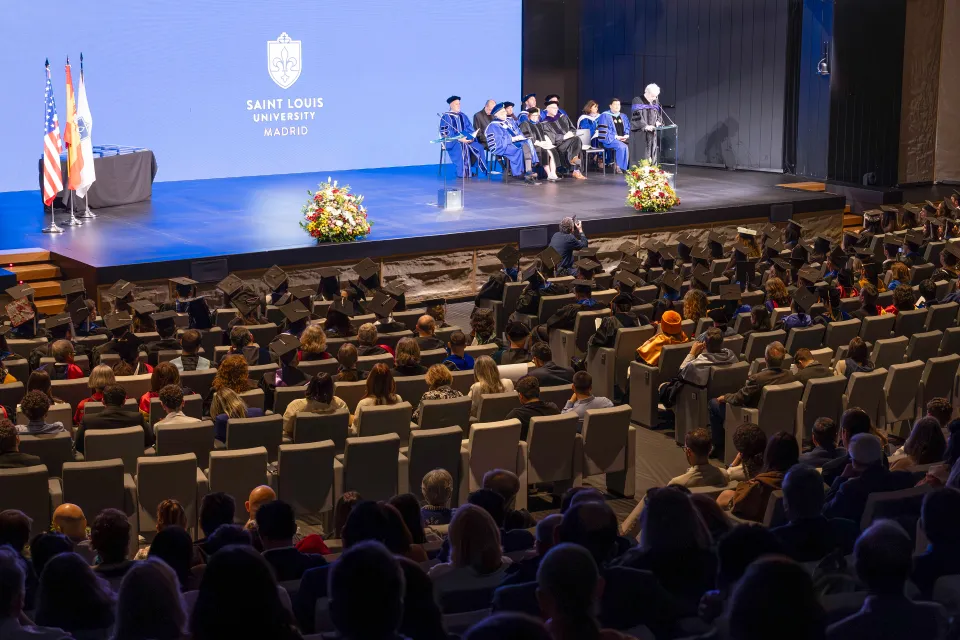 Commencement Ceremony A speaker stands on-stage at a lectern while audience members watch during a commencement ceremony