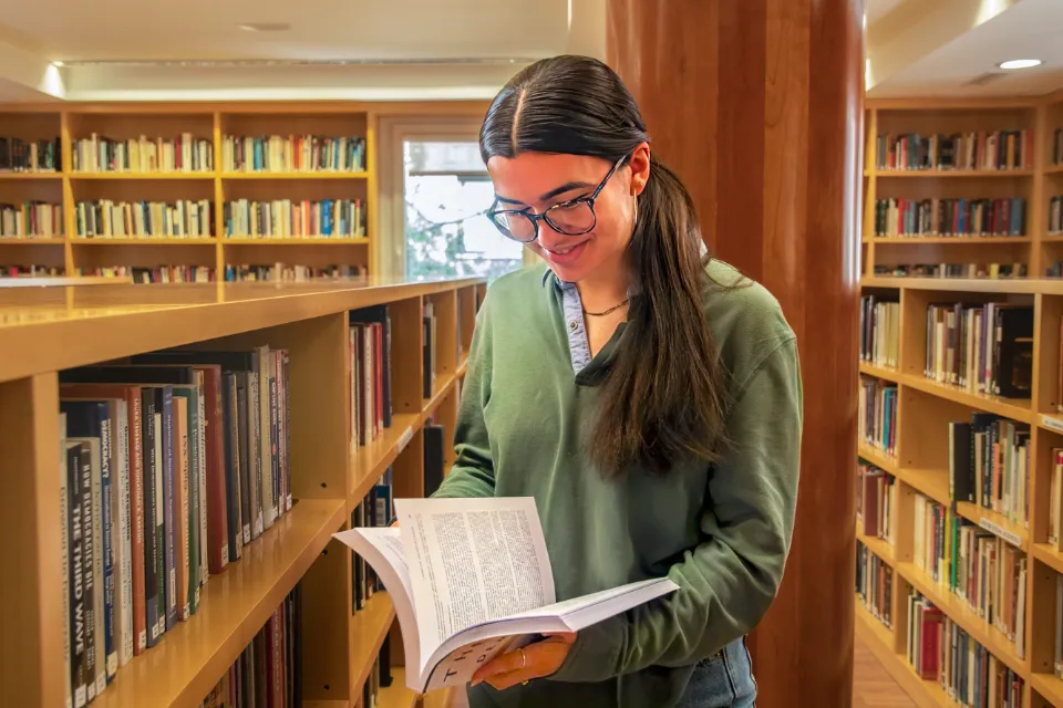 A student sitting at a table with a laptop computer while writing in a notebook.