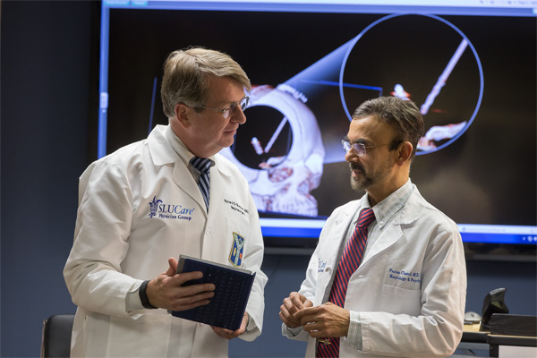 Two male doctors in white coats chat while reviewing information on a clipboard.