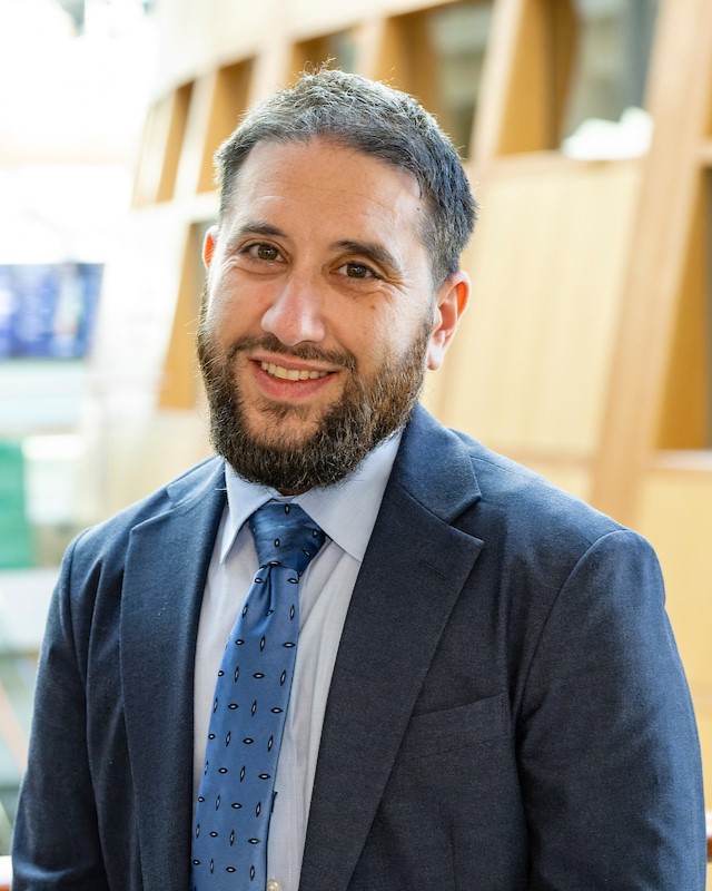 Headshot of Al Miner wearing a light blue dress shirt, cornflower blue tie, and slate blue suitcoat