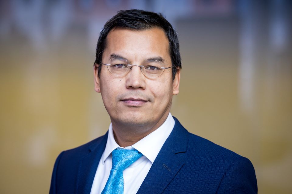 A man wearing glasses, a white shirt, blue business suit and tie.