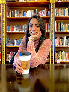 Shabnam Nejat&nbsp; posing with coffee at a table in front of a wall of books