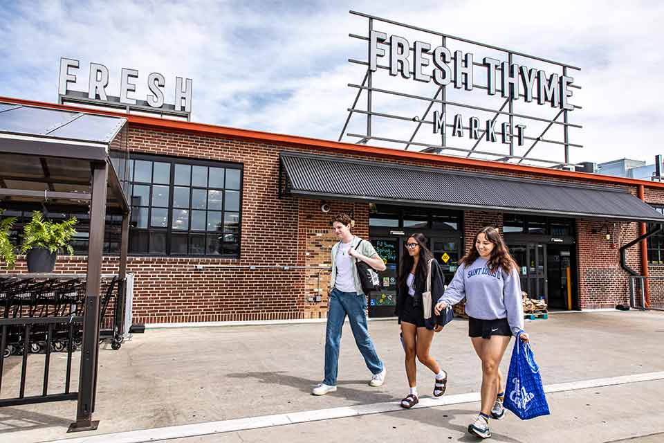 Students leave Fresh Thyme Market while carrying shopping bags.
