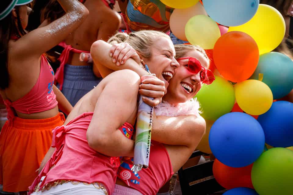 Two students share a hug in front of an assortment of balloons